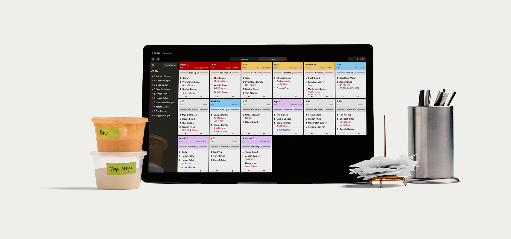 Square Kitchen Display System tablet with order tickets, deli prep containers labeled Cali and Yuzu Mayo, receipt spike, and utensil cup