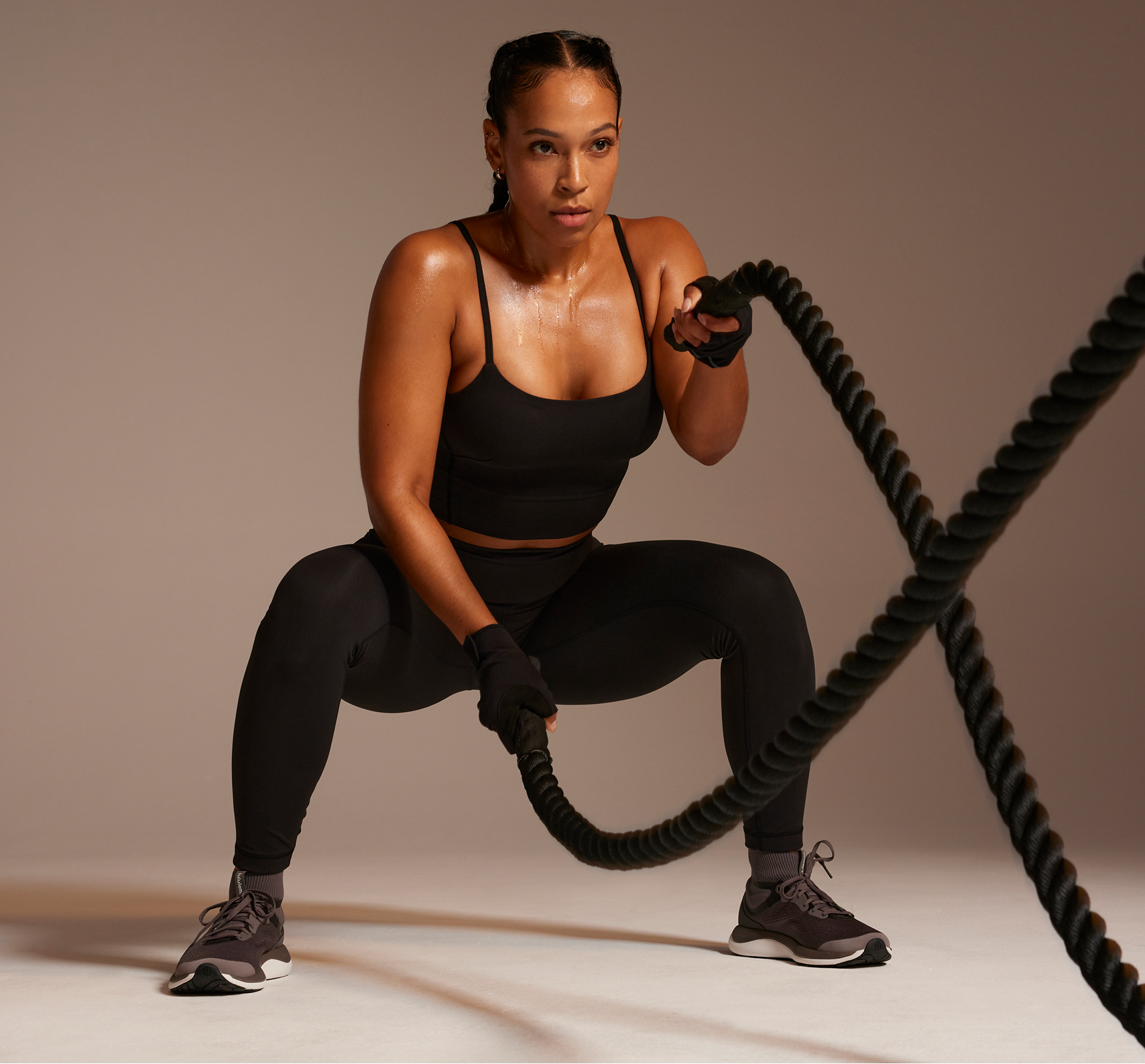 lululemon training — woman in black athletic wear in squat with battle ropes, motion blur, neutral studio